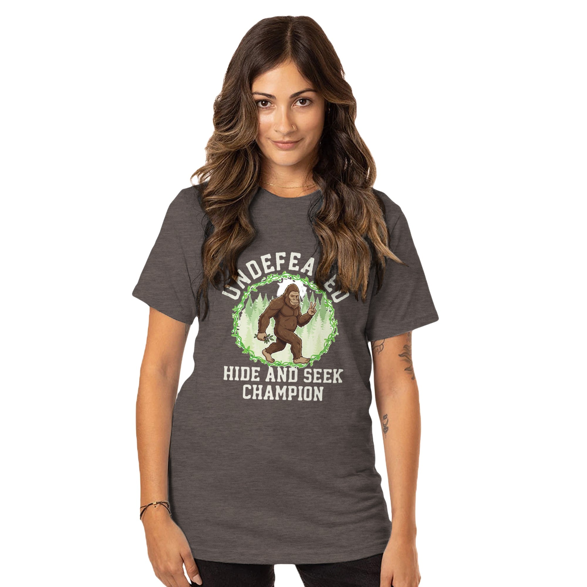 Woman wearing a brown t-shirt with a Big Foot graphic and Undefeated Hide and Seek Champion text on a white background