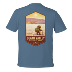 Blue t-shirt with a graphic of a person in a hat and backpack at Death Valley National Park on a white background
